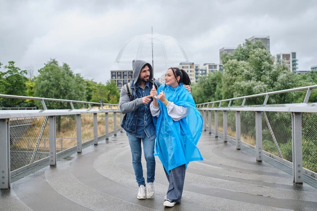 Imagem mostra casal feliz passeando em dia chuvoso, usando capa de chuva, um dos itens para levar em uma viagem por Minas Gerais.